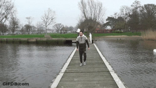 A Man Walking Across A Wooden Bridge Over Water GIF