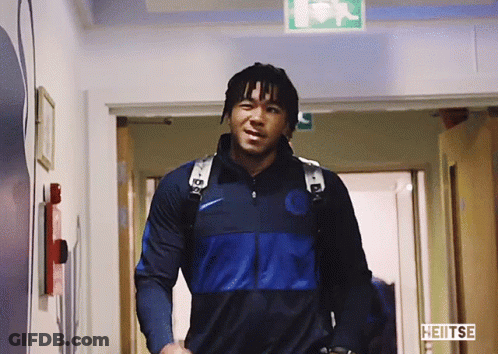 A Man Walking Down A Hallway With Heitse Written On The Bottom Right GIF