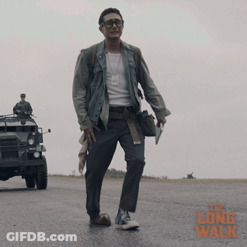 A Man Walking Down A Road With The Long Walk Written In Orange GIF