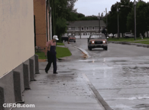 A Man Walking Down A Sidewalk In The Rain With A Red Truck Behind Him GIF