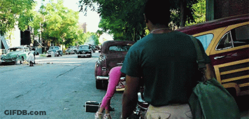 A Man Walking Down A Street With A Green Bag On His Back GIF