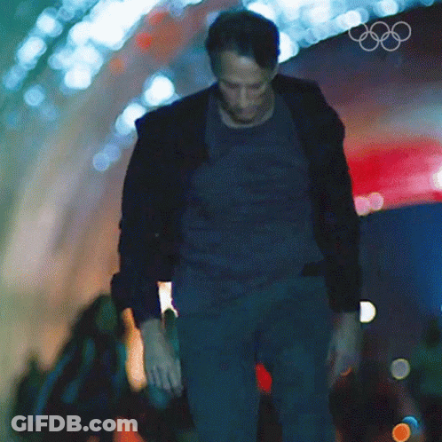 A Man Walking Through A Tunnel With The Olympic Rings On The Wall Behind Him GIF