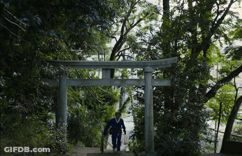 A Man Walking Up A Set Of Stairs Under A Torii Gate With Trees In The Background GIF