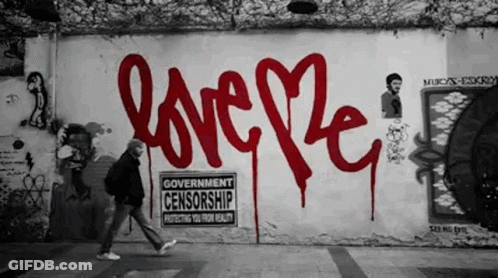 A Man Walks Past A Wall That Has Graffiti On It That Says Love GIF