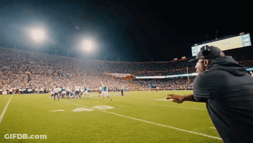 A Man Watches A Football Game In A Stadium With A Scoreboard That Says ' NFL ' On It GIF
