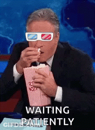 A Man Wearing 3D Glasses Is Eating Popcorn And Saying `` Waiting Patiently '' . GIF
