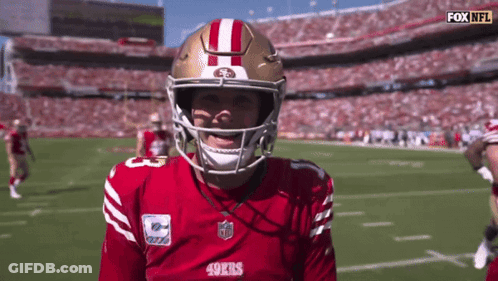 A Man Wearing A 49Ers Jersey And Helmet Stands On A Football Field GIF