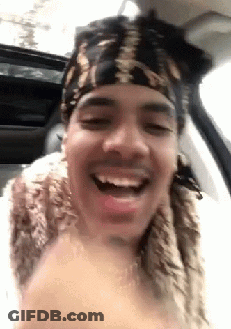 A Man Wearing A Bandana And A Fur Coat Is Sitting In A Car And Smiling . GIF