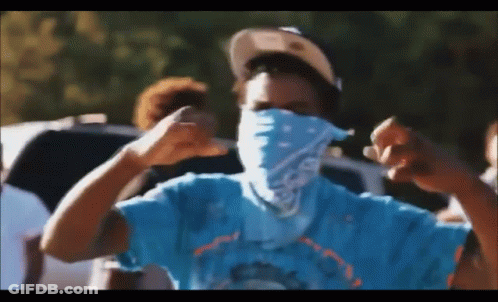 A Man Wearing A Bandana And A Hat Is Making A Fist In The Air . GIF