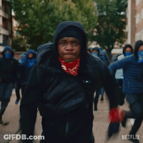 A Man Wearing A Bandana And A Hooded Jacket Is Walking With A Group Of People Wearing Face Masks . GIF