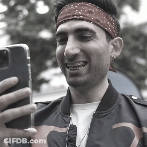A Man Wearing A Bandana And Braces Takes A Selfie With His Phone GIF