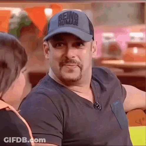 A Man Wearing A Baseball Cap And A Black Shirt Is Sitting At A Table Talking To A Woman . GIF