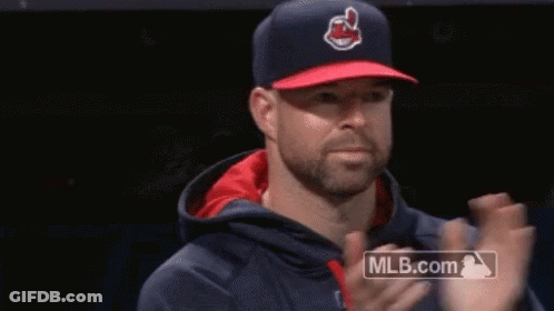 A Man Wearing A Baseball Cap And A Hoodie Is Clapping His Hands . GIF
