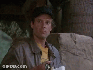 A Man Wearing A Baseball Cap And A Leather Jacket Is Standing Next To A Stone Wall . GIF