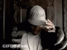 A Man Wearing A Baseball Cap And A Necklace Is Holding A Snake . GIF