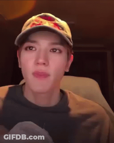 A Man Wearing A Baseball Cap And A Sweatshirt Is Sitting In A Car . GIF