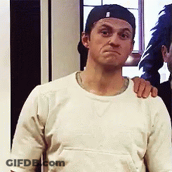 A Man Wearing A Baseball Cap And A White Shirt Is Making A Face GIF