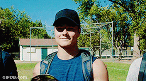 A Man Wearing A Baseball Cap And Sunglasses Is Standing In A Field . GIF