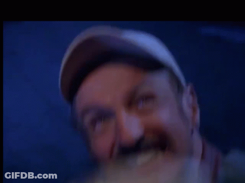 A Man Wearing A Baseball Cap Is Eating A Sandwich In A Blurry Photo . GIF
