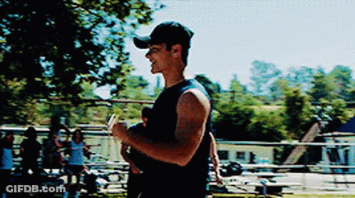 A Man Wearing A Baseball Cap Is Holding A Baby In His Arms . GIF
