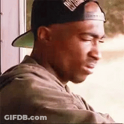 A Man Wearing A Baseball Cap Is Looking Out A Window . GIF