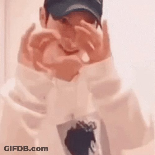 A Man Wearing A Baseball Cap Is Making A Heart With His Hands . GIF
