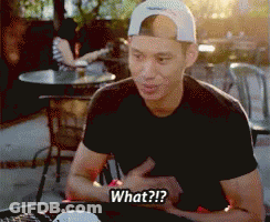 A Man Wearing A Baseball Cap Is Sitting At A Table And Says " What " GIF