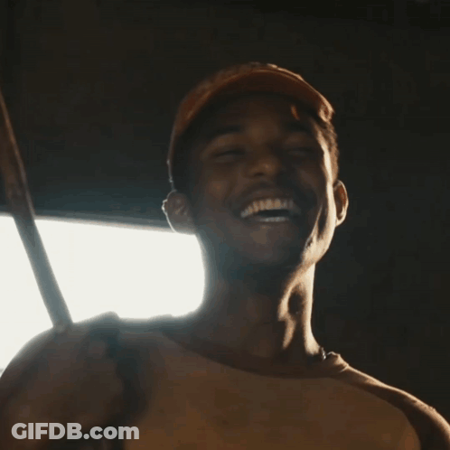 A Man Wearing A Baseball Cap Is Smiling And Holding A Stick GIF