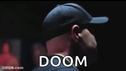 A Man Wearing A Baseball Cap Is Standing In A Dark Room With The Word Doom Behind Him . GIF