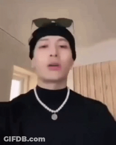 A Man Wearing A Beanie And A Necklace Is Making A Face . GIF