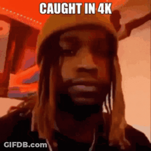 A Man Wearing A Beanie And A Necklace With The Words `` Caught In 4K '' Written On It . GIF