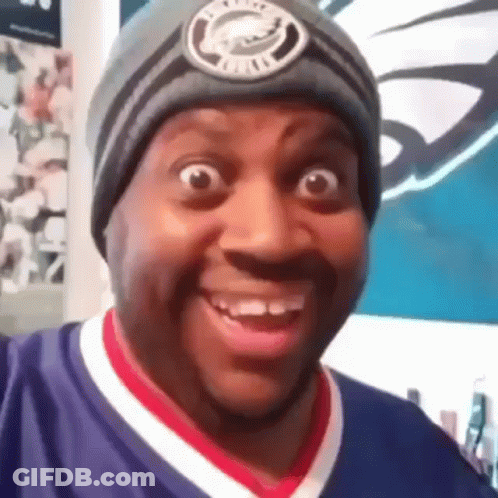 A Man Wearing A Beanie And A Purple Shirt Is Smiling . GIF
