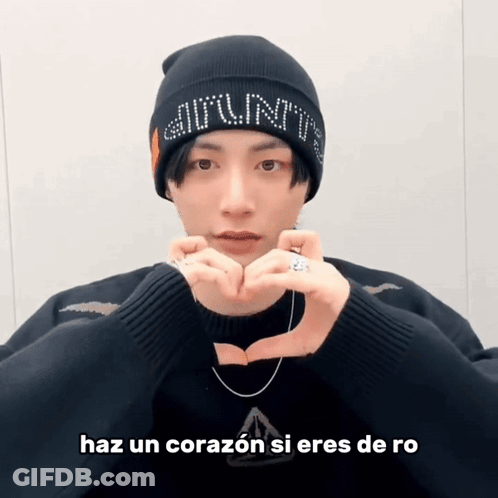 A Man Wearing A Beanie And A Sweater Makes A Heart Shape With His Hands GIF