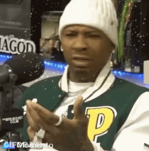 A Man Wearing A Beanie And A Varsity Jacket Is Clapping His Hands . GIF