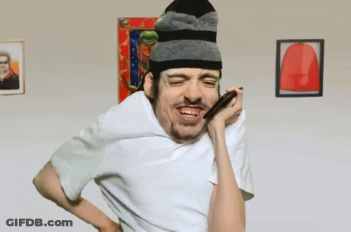 A Man Wearing A Beanie And A White Shirt Is Blowing Into A Straw GIF
