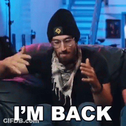 A Man Wearing A Beanie And Scarf Is Sitting On A Couch With The Words `` I 'M Back '' . GIF