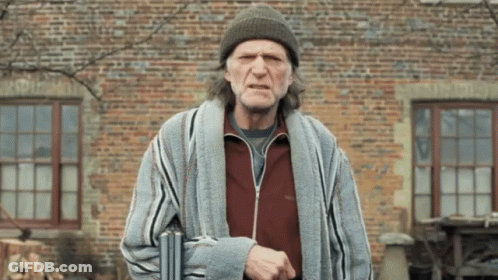 A Man Wearing A Beanie And Striped Robe Is Standing In Front Of A Brick Wall GIF