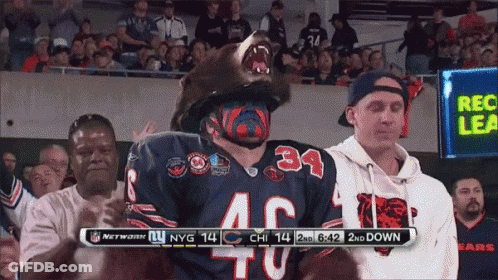 A Man Wearing A Bear Mask Is Standing In Front Of A Scoreboard That Says Nfl Network GIF