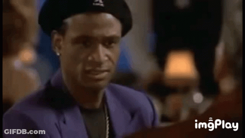 A Man Wearing A Beret And A Purple Suit Is Smiling While Talking To Another Man . GIF
