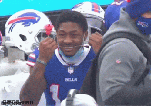 A Man Wearing A Bills Jersey Is Smiling And Putting On A Mask GIF