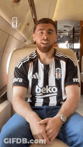 A Man Wearing A Black And White Beko Shirt Sits On A Plane GIF