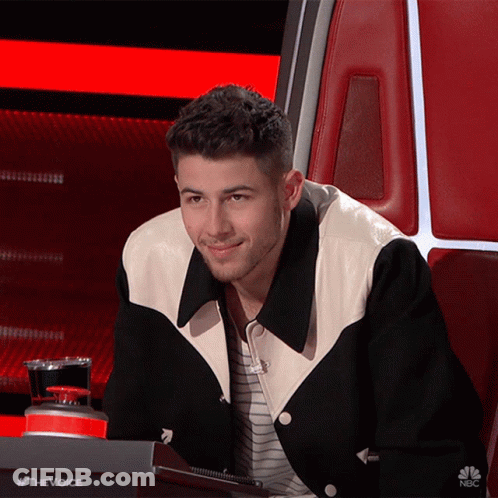 A Man Wearing A Black And White Jacket Is Sitting In A Chair With The Words #Thevoice On The Bottom GIF