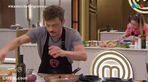 A Man Wearing A Black Apron With The Letter M On It GIF
