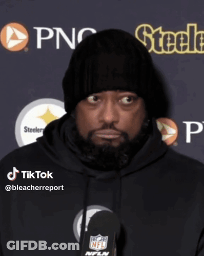 A Man Wearing A Black Beanie And A Black Hoodie Is Talking Into A Microphone GIF