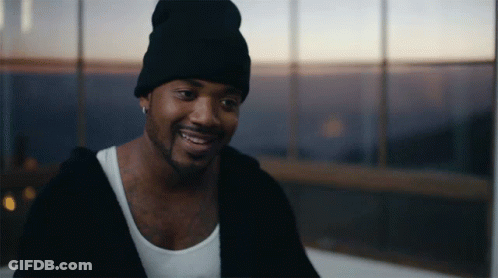 A Man Wearing A Black Beanie And A White Tank Top Smiles In Front Of A Window GIF