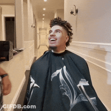 A Man Wearing A Black Cape With The Letter L On It Is Smiling GIF