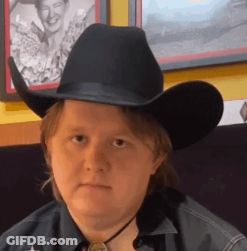 A Man Wearing A Black Cowboy Hat And A Star On His Shirt GIF
