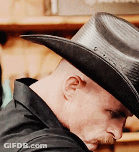A Man Wearing A Black Cowboy Hat Is Looking Down GIF