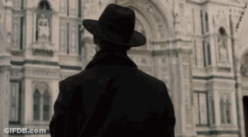 Man In Black Hat And Coat In Front Of Building GIF