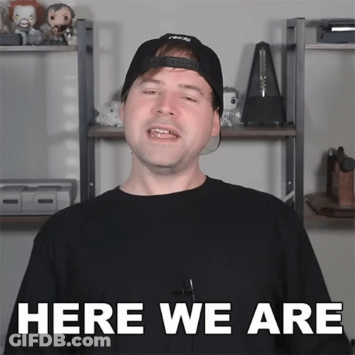 A Man Wearing A Black Hat And A Black Shirt Says Here We Are GIF